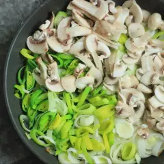Kroimy pieczarki i pora na patelni, przygotowując składniki do pysznego sosu pieczarkowego.