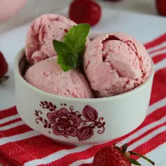 Pyszne lody truskawkowe w miseczce, ozdobione miętą. Idealne na lato, pokazują, jak zrobić lody truskawkowe.