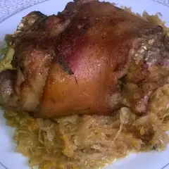Pyszna, gotowana golonka w kapuście kiszonej, podana na talerzu z ozdobnym wzorem.