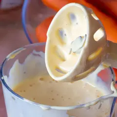 Przygotowanie domowego majonezu. Blender zanurzony w kremowej emulsji, w tle pomarańczowe marchewki.