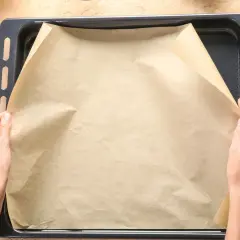 Dłonie układają papier do pieczenia na blasze.