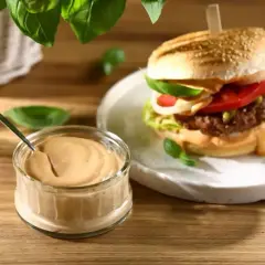 Pyszny sos do burgera w słoiczku obok soczystego burgera z pomidorem i sałatą. Idealny dodatek do każdej kanapki.