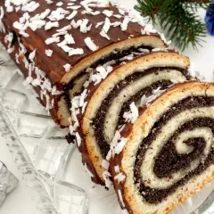 Stary przepis na makowiec, udekorowany czekoladą i wiórkami kokosowymi, prezentuje się świątecznie obok choinkowych gałązek i prezentów.