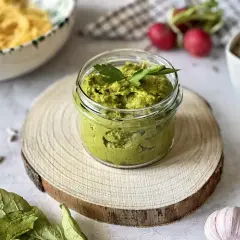 Pesto z liści rzodkiewki w słoiczku, ozdobione natką pietruszki. Obok makaron, rzodkiewki i czosnek.