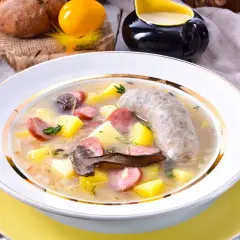 Babcina zalewajka przepis: sycąca zupa z ziemniakami, kiełbasą i grzybami, podana w białej misce ze złotym rantem.