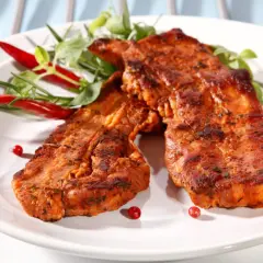Dwa soczyste kawałki boczek z grilla, przyprawione i udekorowane papryczkami chili i zieleniną.