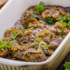 Pyszny kotlet husarski duszony z cebulą i ziołami, podany w białej brytfannie.