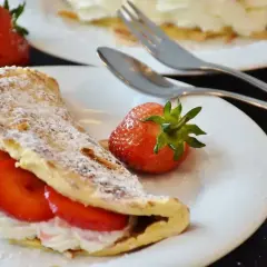 Słodki omlet z bitą śmietaną i truskawkami, posypany cukrem pudrem. Idealny przepis na omlet na słodko.