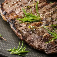 Soczysty stek wieprzowy, grillowany z ziołami i grubą solą, prezentuje się apetycznie na ciemnej płycie.