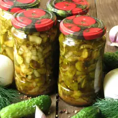 Słoiki z ogórkami w curry ze skórką, otoczone świeżymi ogórkami, cebulą, czosnkiem i koprem.