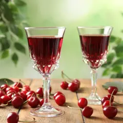 Dwa kieliszki z rubinową nalewką z wiśni na spirytusie, obok świeże wiśnie na drewnianym stole. Szybka nalewka z wiśni na spirytusie gotowa do degustacji.