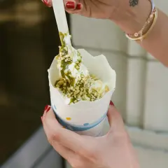 Ręce trzymają kubek z lodami mcflurry pistacjowe, posypane orzeszkami i polane zielonym sosem.