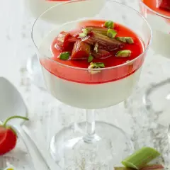 Panna cotta z rabarbarem i pistacjami w kieliszku. Słodki deser z rabarbarem, ozdobiony zielonymi orzeszkami.