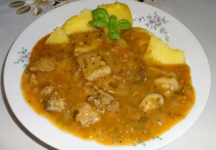 Pyszny sos do ziemniaków z kawałkami mięsa i warzyw, udekorowany listkiem bazylii.