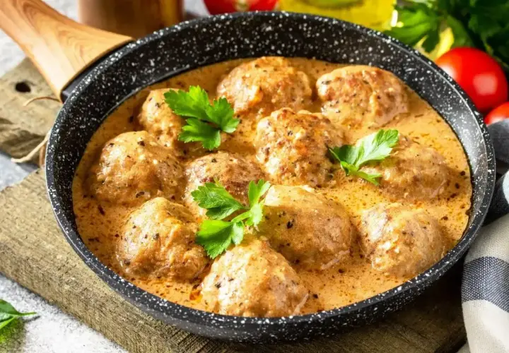 Pulpeciki w kremowym sosie, udekorowane natką pietruszki, gotowe do podania. Pyszny sos do pulpetów kusi aromatem.