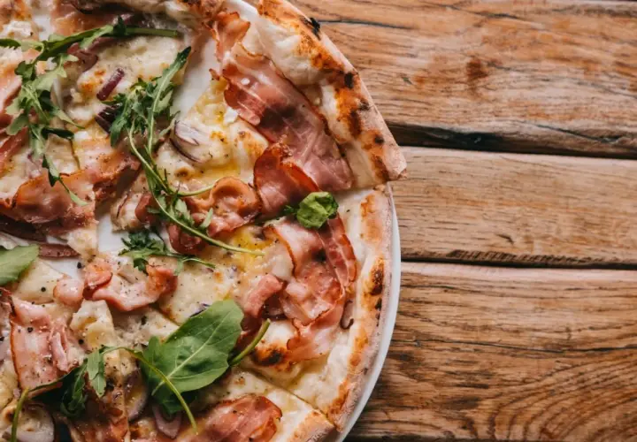 Pyszna pizza carbonara z chrupiącym boczkiem i rukolą, podana na drewnianym stole.