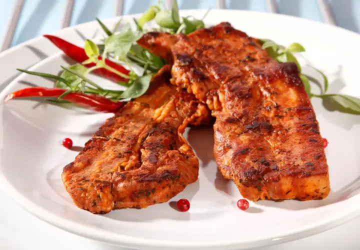 Dwa soczyste kawałki boczek z grilla, przyprawione i udekorowane papryczkami chili i zieleniną.