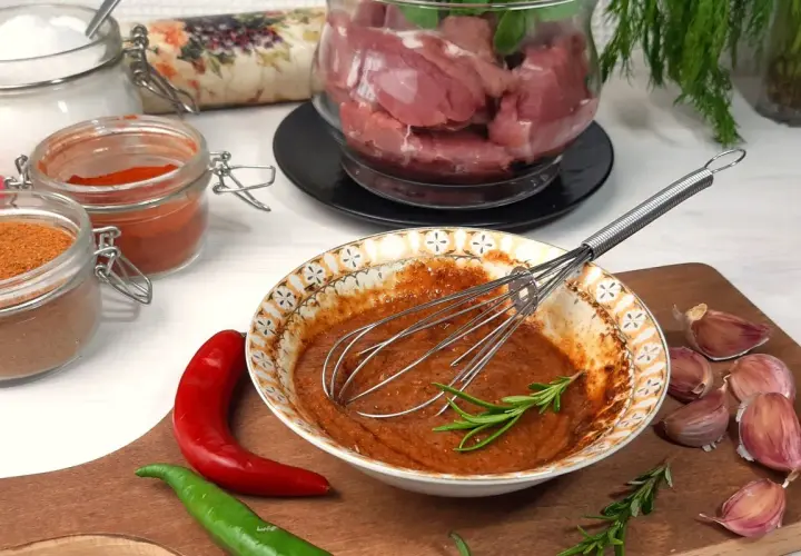Przygotowanie marynaty do polędwiczki wieprzowej: miska z przyprawami, chili, czosnek i mięso w tle.