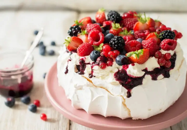 Beza pavlova która zawsze wychodzi, udekorowana bitą śmietaną i mnóstwem świeżych owoców leśnych.