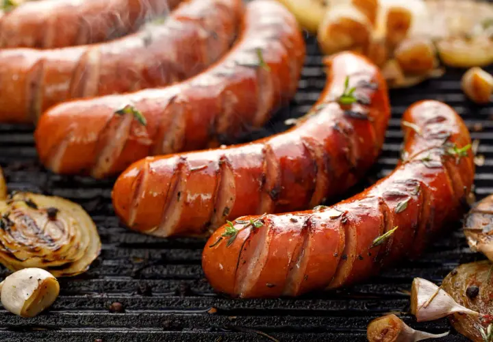Soczysta kiełbasa z grilla, parująca i pachnąca ziołami. Obok grillowana cebula i czosnek. Idealna na letnie wieczory, choć warto pamiętać o jej kcal.