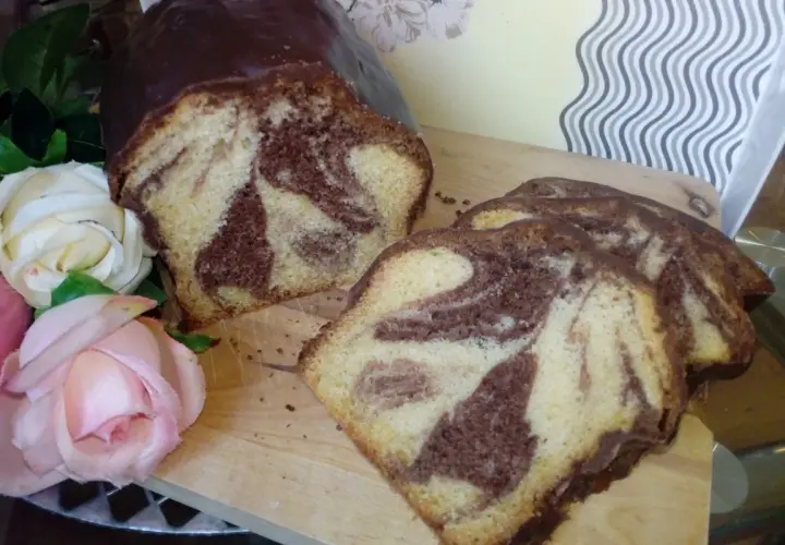 Wilgotna babka marmurkowa na oleju, oblana czekoladą, prezentuje się apetycznie obok róż.