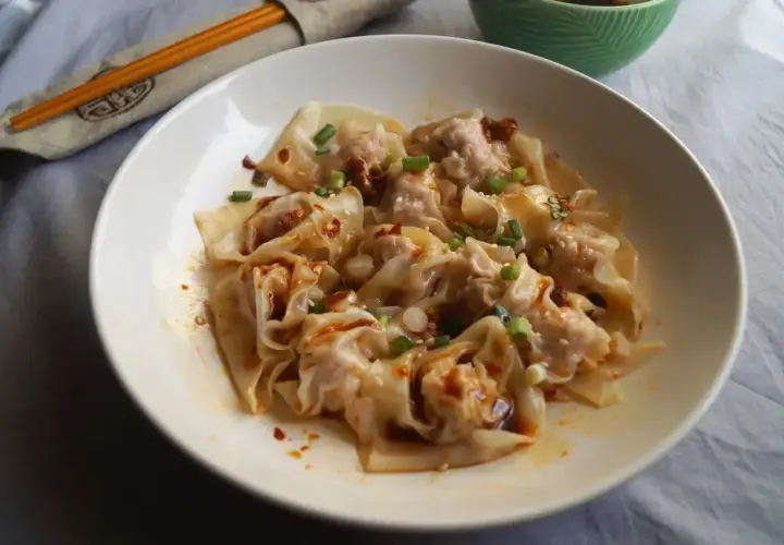 Pyszne ciasto wonton w pikantnym sosie, posypane szczypiorkiem i sezamem. Obok pałeczki w etui.