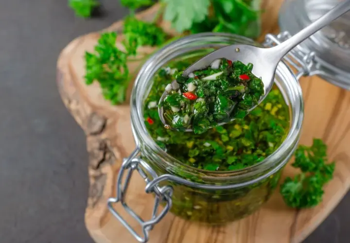 Łyżka z aromatycznym chimichurri, pełnym ziół i papryczki, nad słoikiem.