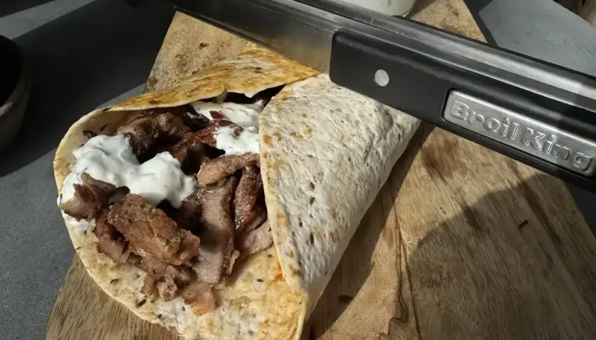 Pyszny kebab kryspinów z jakim sosem, gotowy do podania. Mięso soczyste, zawinięte w tortillę, polane białym sosem.