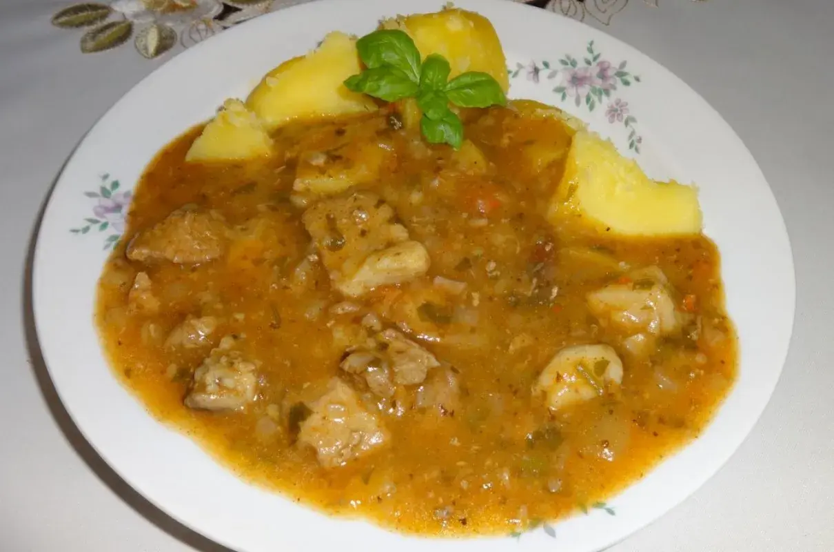 Pyszny sos do ziemniaków z kawałkami mięsa i warzyw, udekorowany listkiem bazylii.