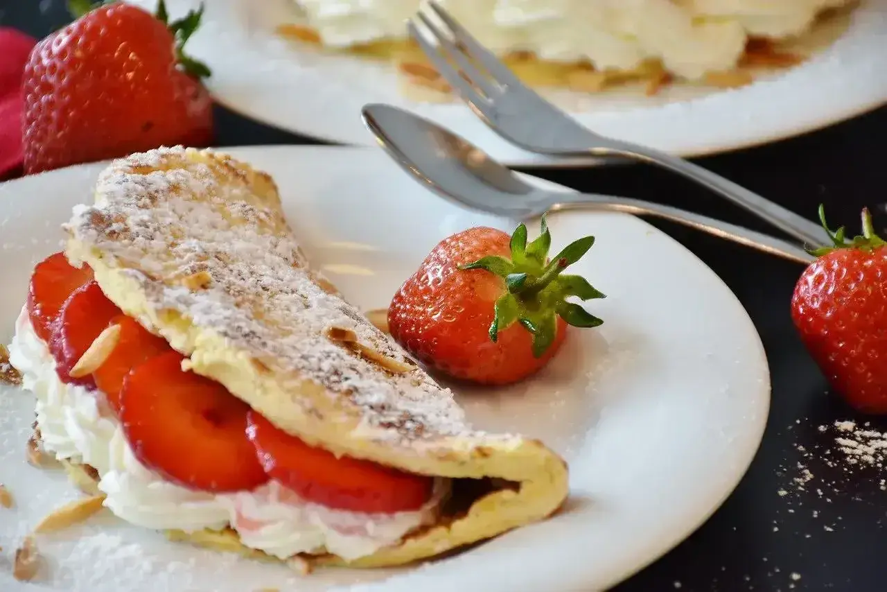 Słodki omlet z bitą śmietaną i truskawkami, posypany cukrem pudrem. Idealny przepis na omlet na słodko.