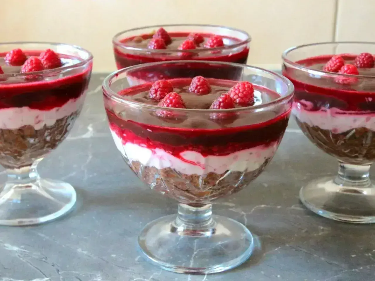 Pyszny deser z mascarpone i galaretką malinową, udekorowany świeżymi malinami, podany w eleganckich pucharkach.