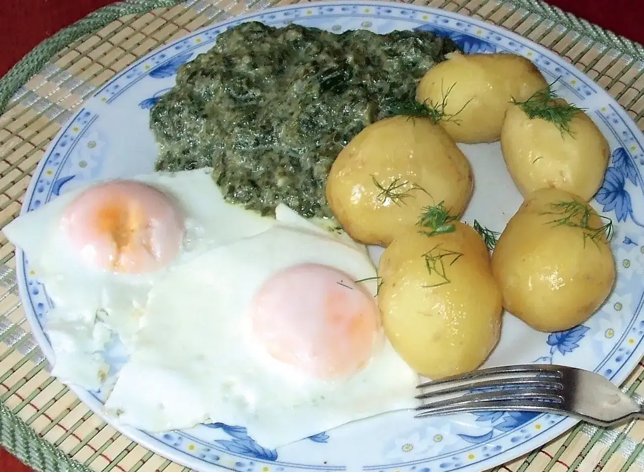 Pyszny szpinak przepis na talerzu z jajkami sadzonymi i młodymi ziemniaczkami.