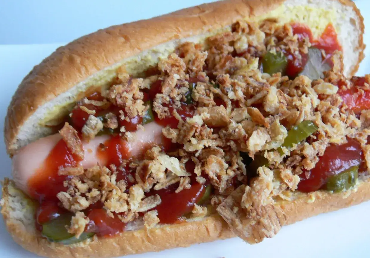 Pyszny hot dog francuski z chrupiącą cebulką, ogórkiem konserwowym i sosem.