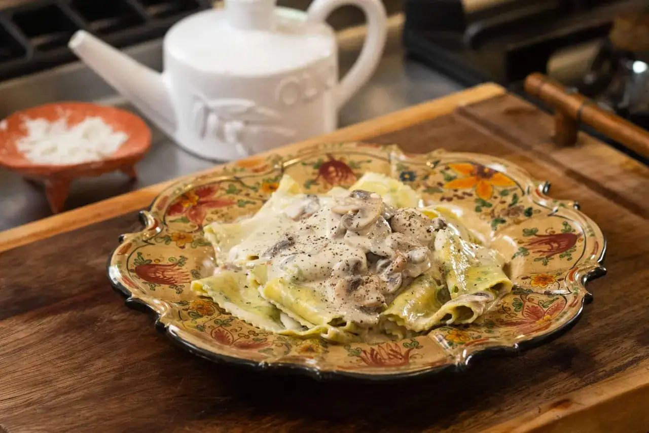 Ravioli z grzybami w kremowym sosie śmietanowym, podane na ozdobnym talerzu.